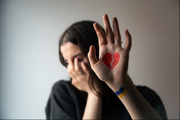 A Ukrainian girl with a broken heart and a flag drawn on her hand, pain for Ukraine, the concept of the war in Ukraine.